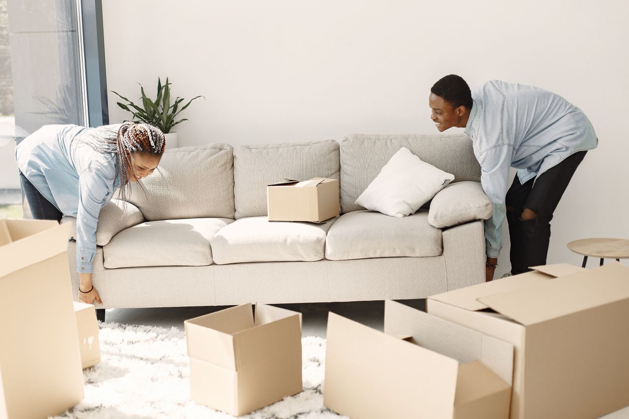 A happy couple arranging a sofa in their new home, with moving boxes all around them.